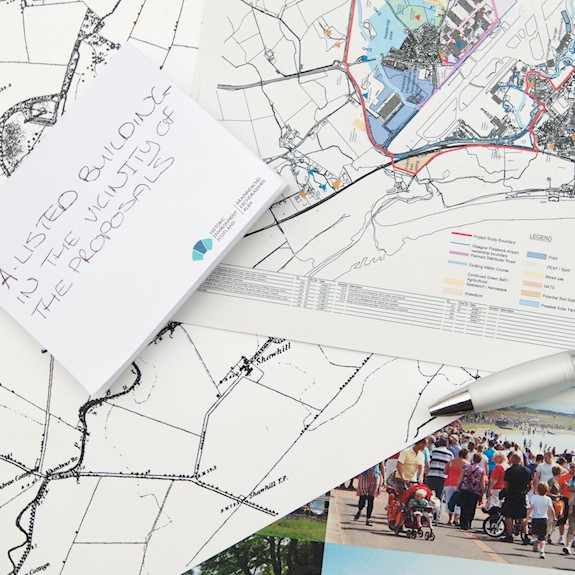 A collage of maps and planning documents sitting on a table, with a pen. Some of the maps are historic, others modern Ordnance Survey versions.