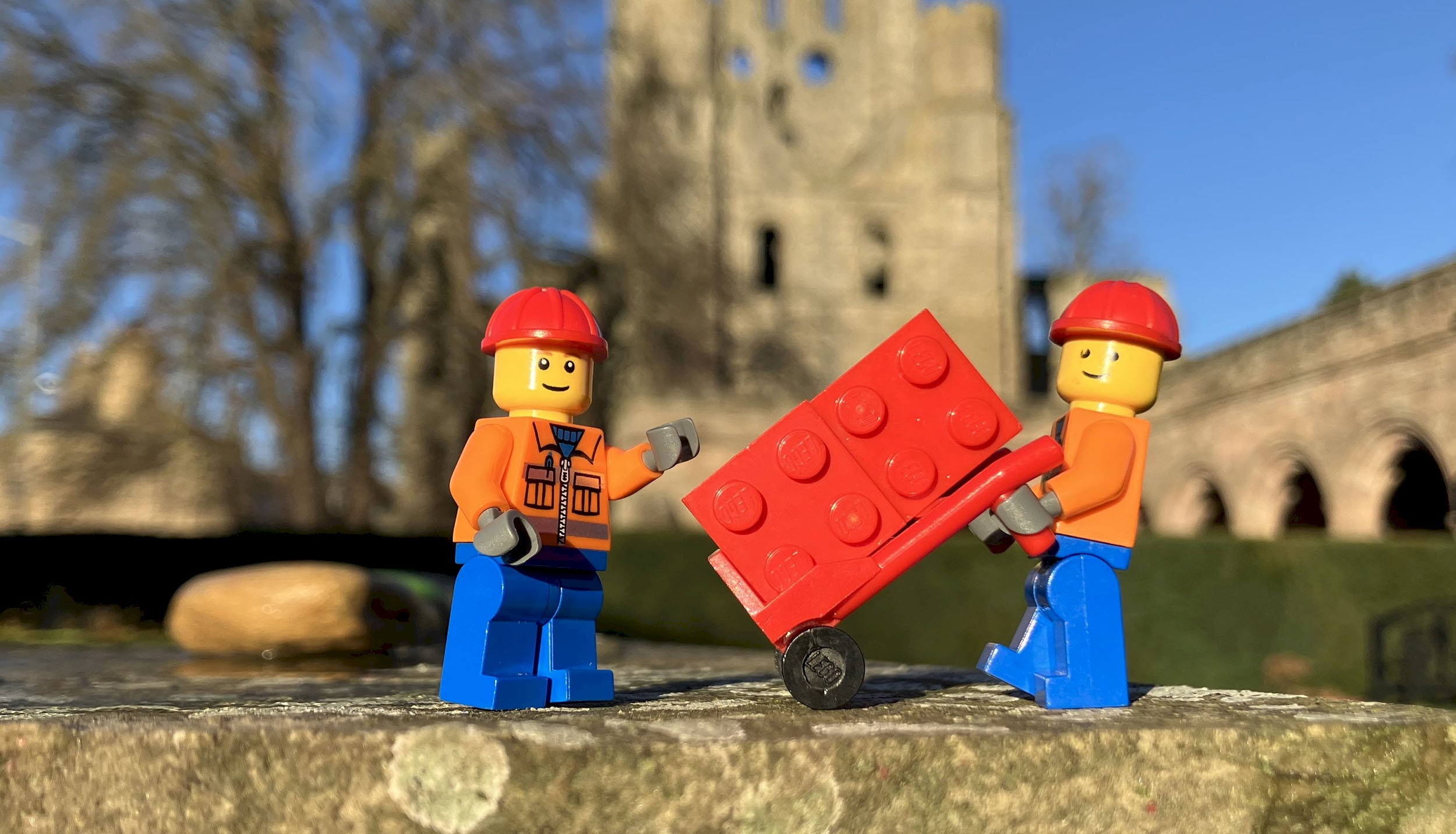 Two lego figures, one with a trolley pulling lego bricks 