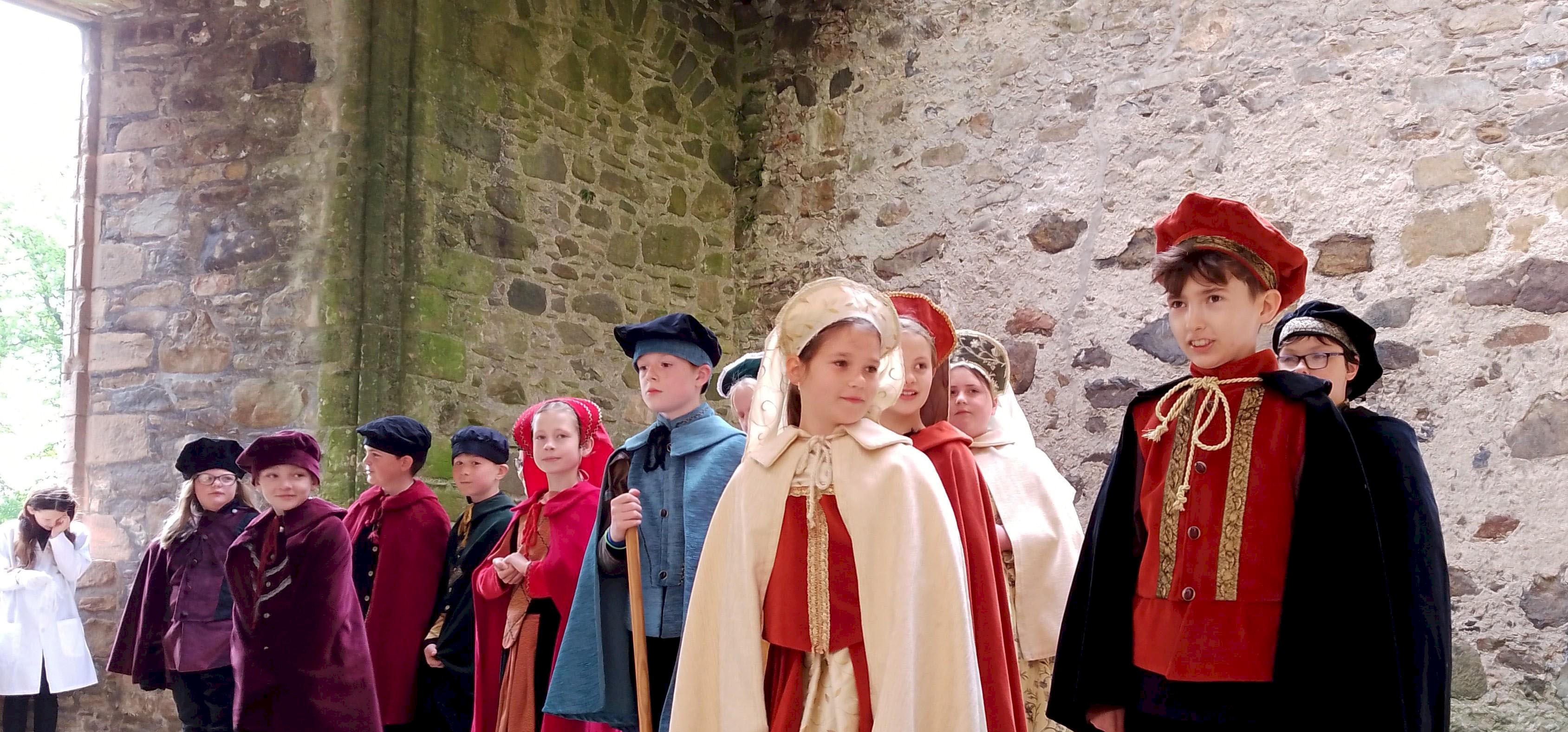 Junior tour guides dressed in period costume and standing in Huntly Castle Great Hall