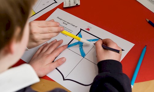A boy drawing on paper that has an outline of a shield