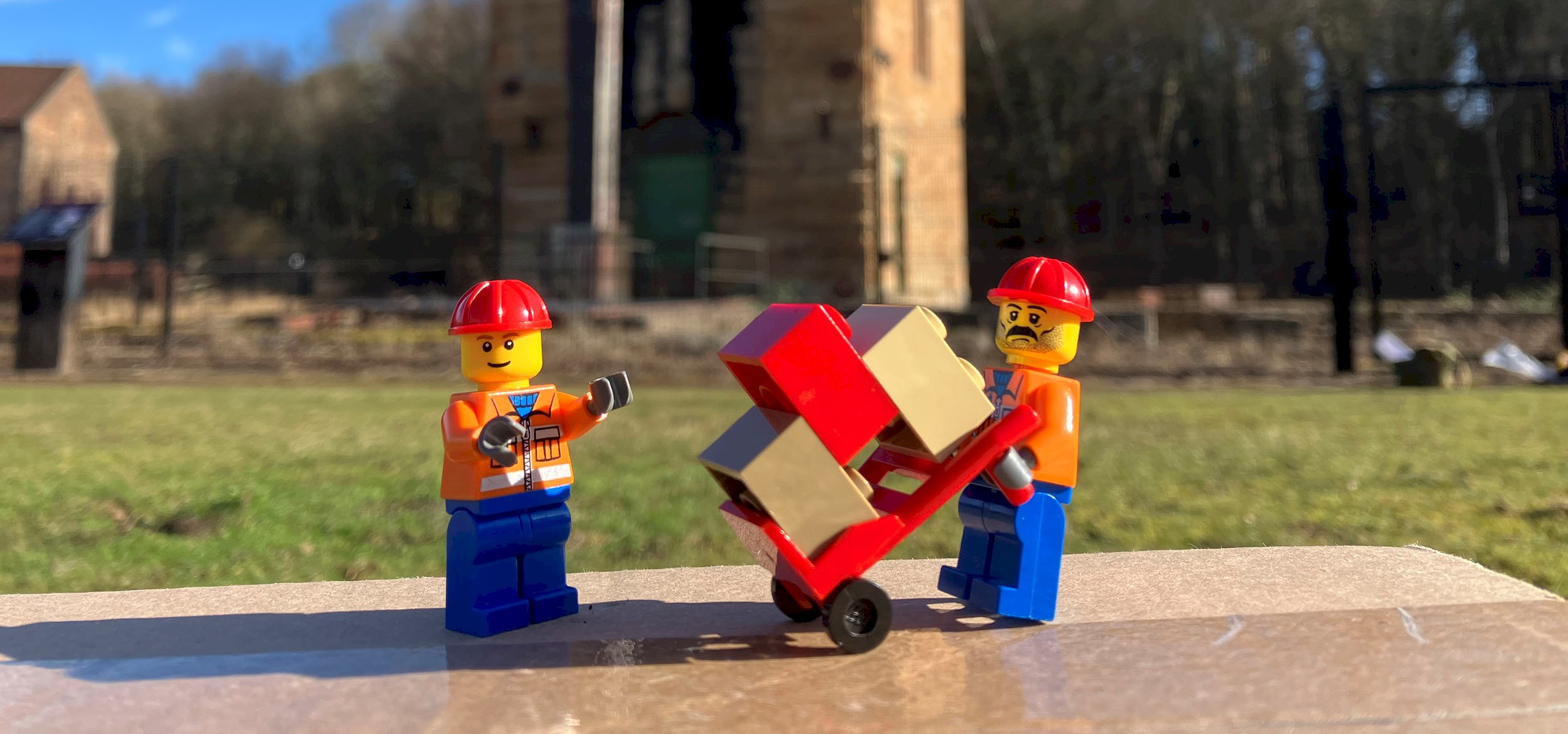 Two Lego figures holding bricks. Landscape and a monument is behind them.
