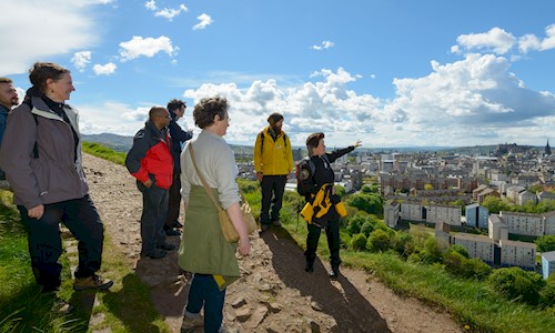 A group of people standing on a hill on a sunny warm day looking out over a city