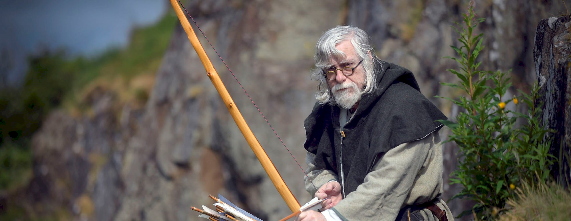 A costumed performer as a Fletcher (or Arrow Maker) holding a bow and arrow