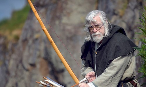 A costumed performer as a Fletcher (or Arrow Maker) holding a bow and arrow