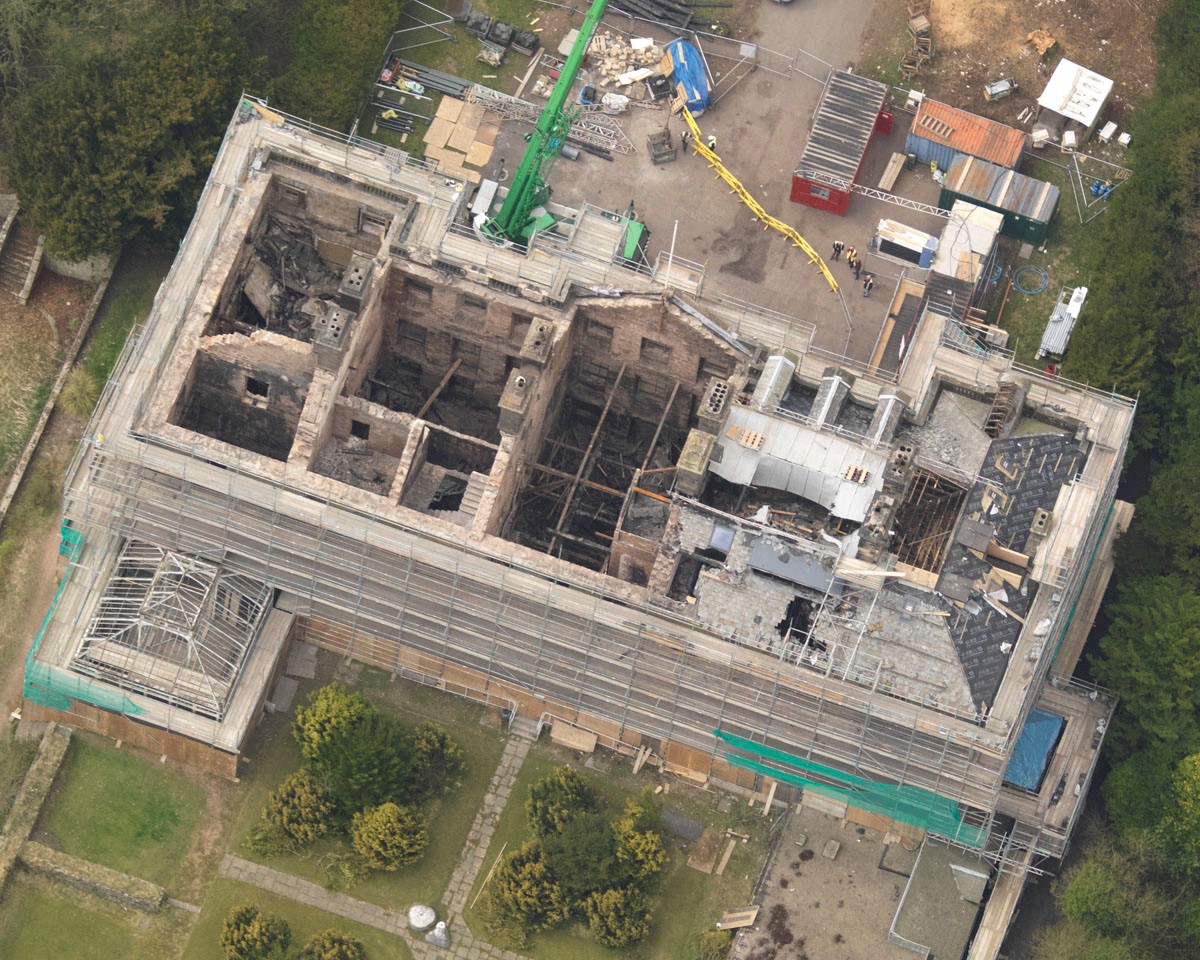 A traditional stone building badly damaged by fire with no roof, crumbling walls and surrounded by scaffolding 