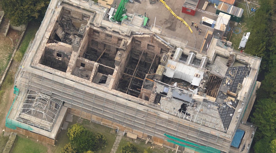 A traditional stone building badly damaged by fire with no roof, crumbling walls and surrounded by scaffolding