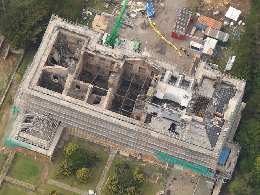 A traditional stone building badly damaged by fire with no roof, crumbling walls and surrounded by scaffolding