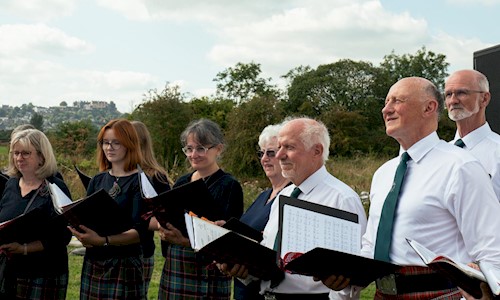 A choir outdoors singing with lots of greenery behind them