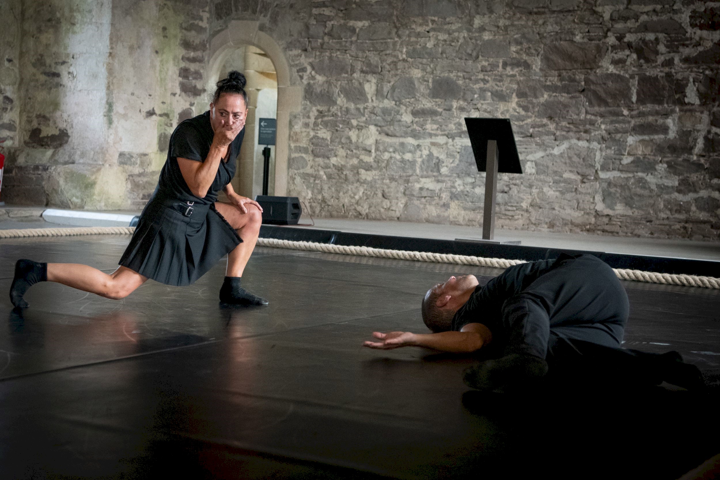Two performers on a stage, one person is laying on the floor and the other is gasping. 