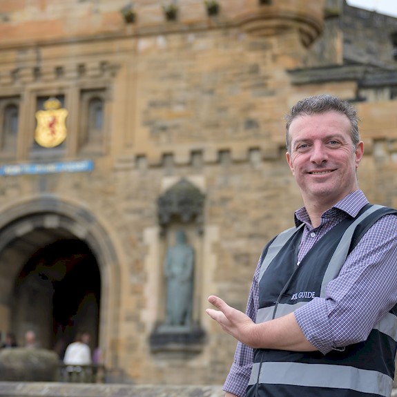BSL guide Gordon Hay smiling and pointing towards the entrance of Edinburgh Castle