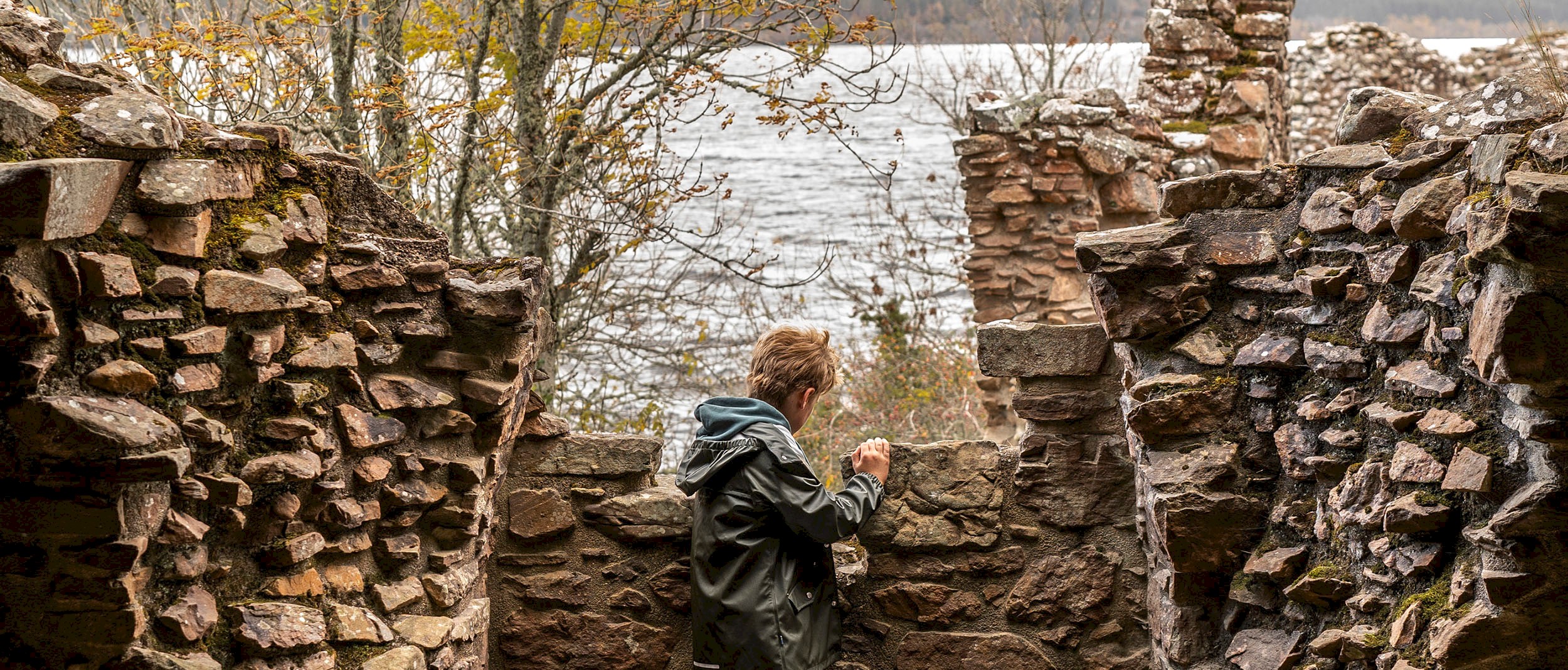 A young person looking out from part of a ruinous castle towards a large loch