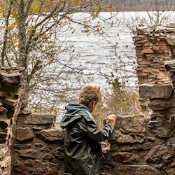 A young person looking out from part of a ruinous castle towards a large loch