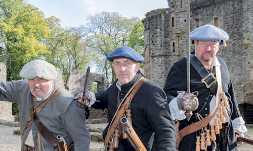 Three costumed performers in the grounds of Huntly Castle brandishing a knife, musket and sword 
