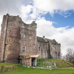 A tall grey castle surrounded by temporary fencing, with the entrance way boarded up with scaffolding.