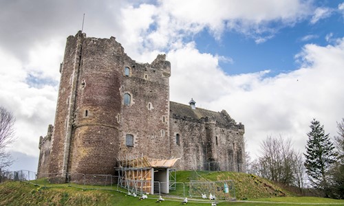 A tall grey castle surrounded by temporary fencing, with the entrance way boarded up with scaffolding.