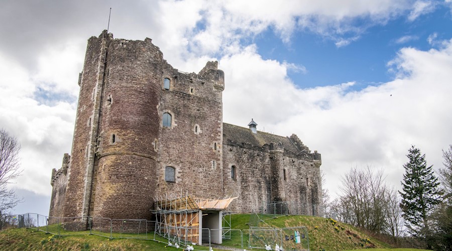 A tall grey castle surrounded by temporary fencing, with the entrance way boarded up with scaffolding.