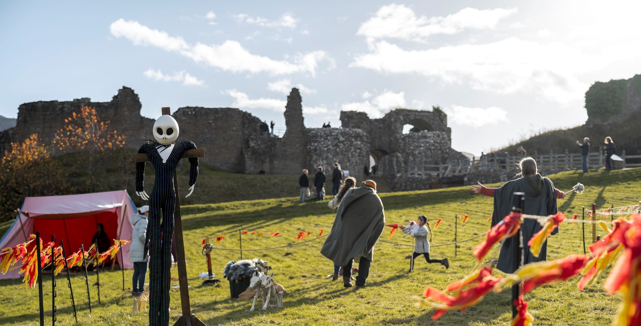 The grounds of a castle ruin with a ghostly scarecrow and people milling around the grounds.