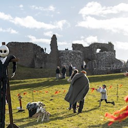 The grounds of a castle ruin with a ghostly scarecrow and people milling around the grounds.