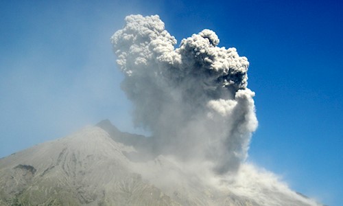 A volcano erupting with grey/white smoke and a very blue sky