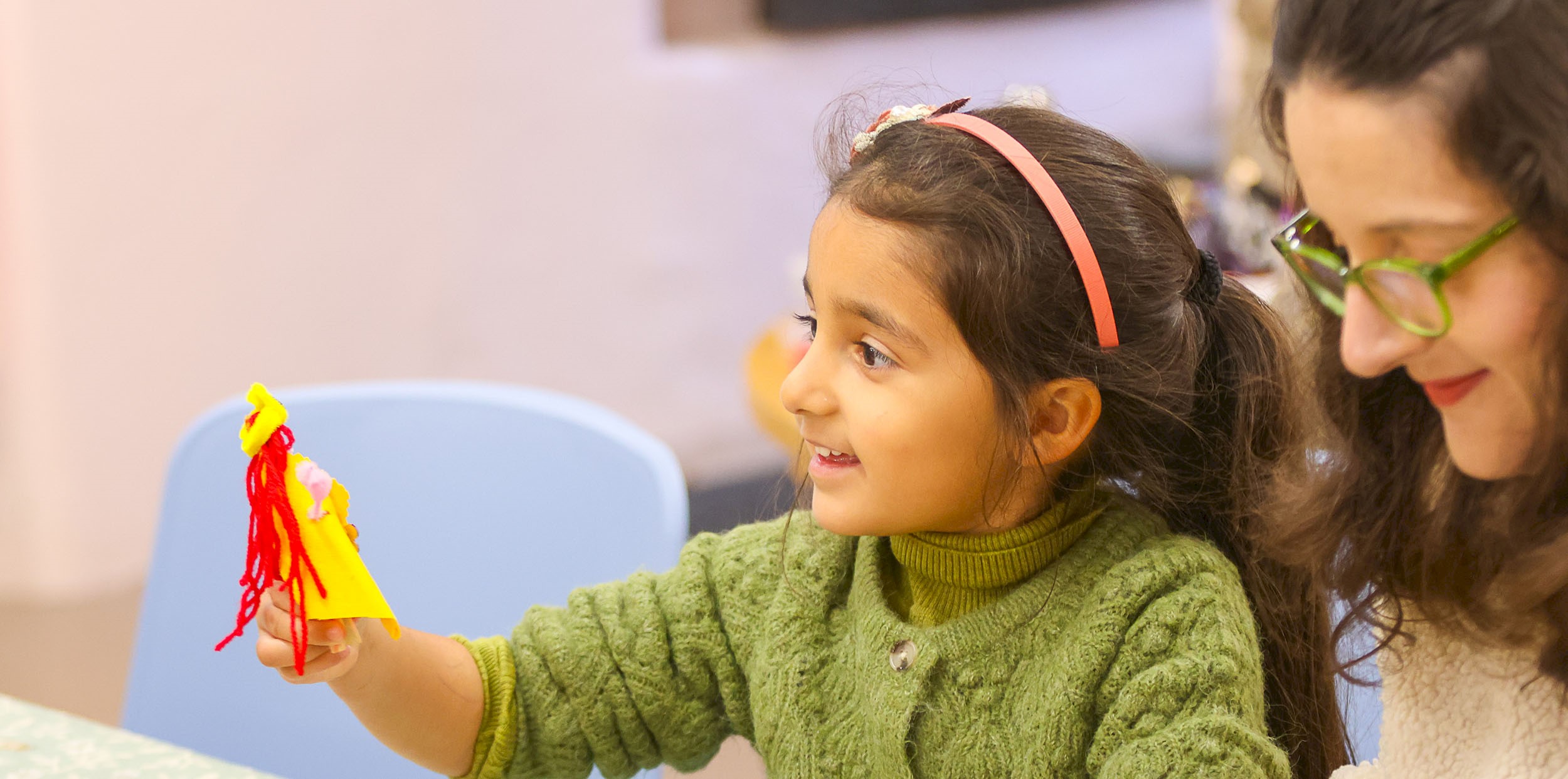 A girl with a big smile holding up a peg doll that she's made