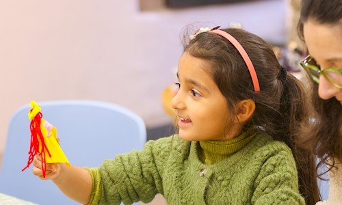 A girl with a big smile holding up a peg doll that she's made
