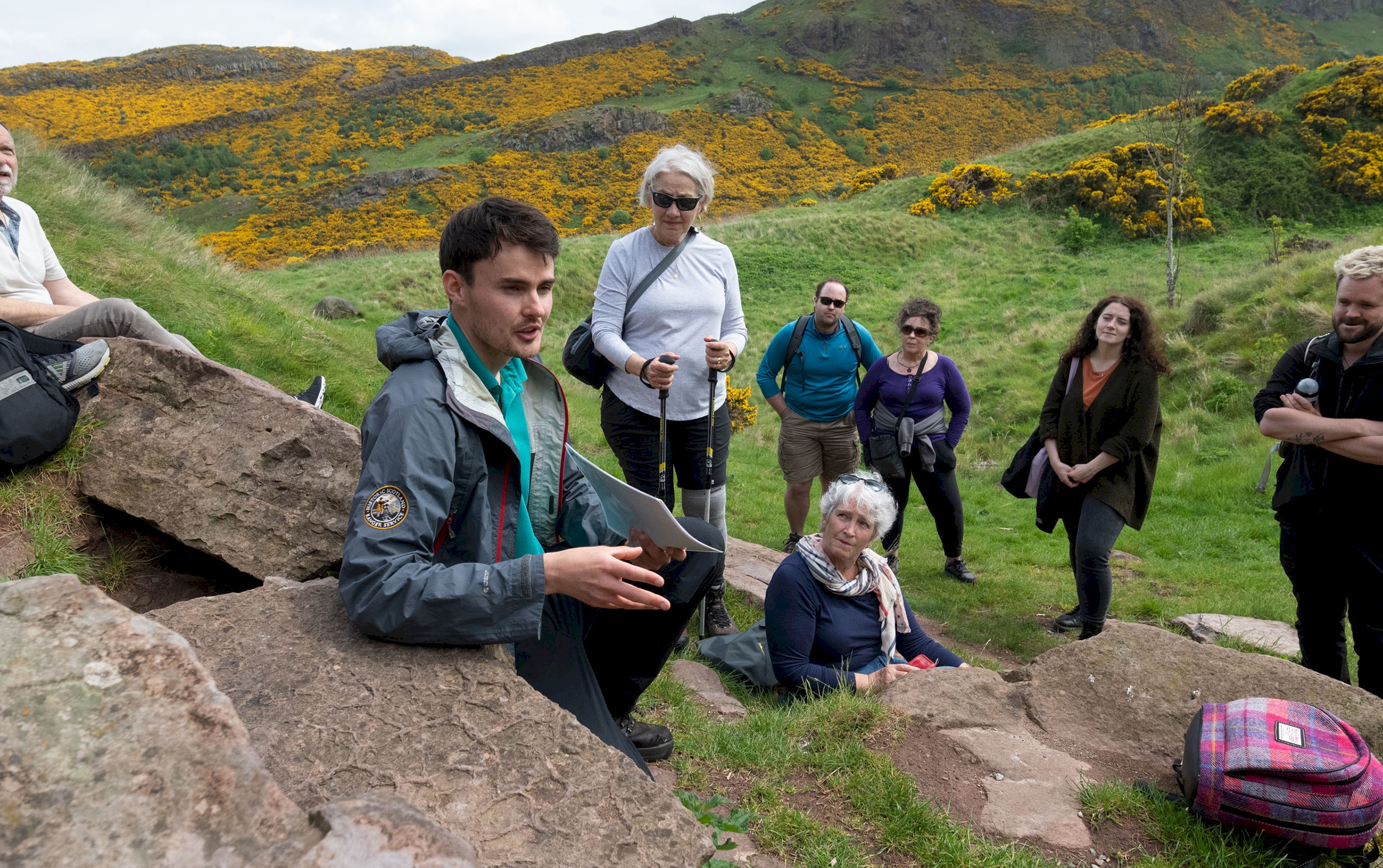 A group of people with a Ranger enjoying a rest on a walking tour of Holyrood Park