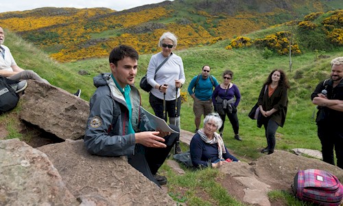 A group of people with a Ranger enjoying a rest on a walking tour of Holyrood Park