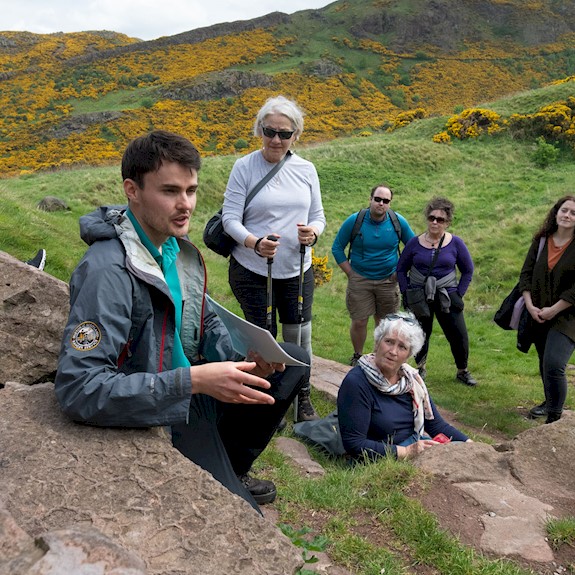A group of people with a Ranger enjoying a rest on a walking tour of Holyrood Park