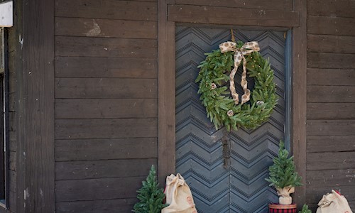 A wooden building with a wreath on the door and some small Christmas trees and present sacks on the ground