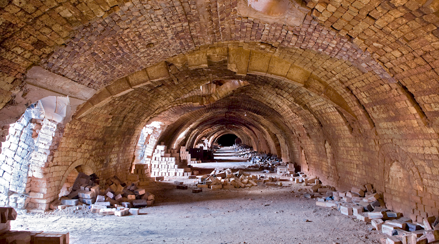 An arched, bricked corridor with bricks lying on the sides. 