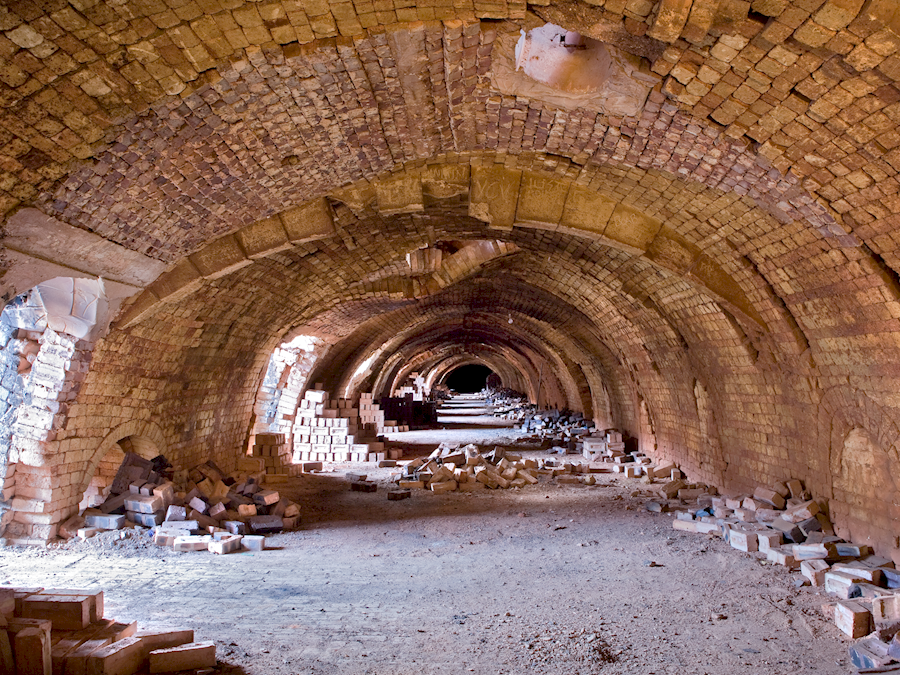 An arched, bricked corridor with bricks lying on the sides. 