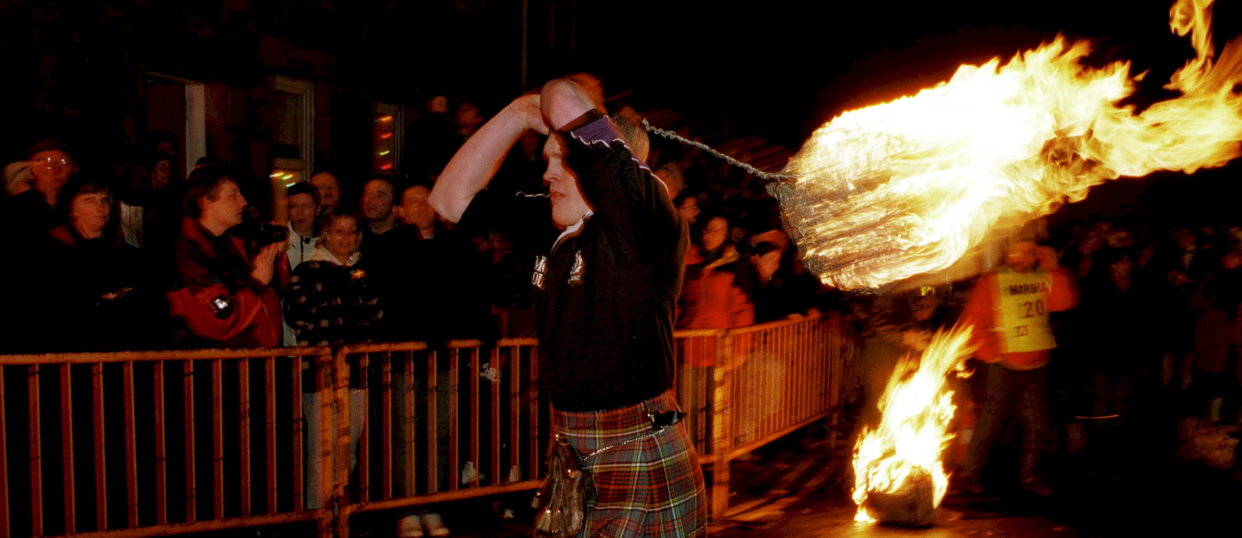 A man in a kilt swinging a flaming fireball on a wire handle. A traditional ceremony held in Stonehaven on New Year's Eve
