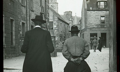 A black and white photo with two men walking through a street 