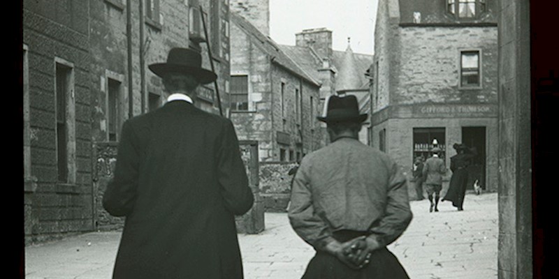 A black and white photo with two men walking through a street 