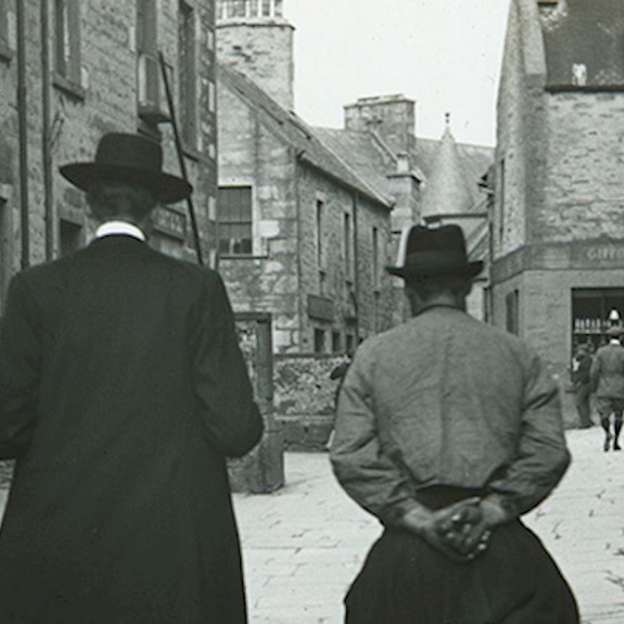 A black and white photo with two men walking through a street 