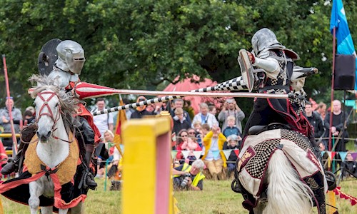 Costumed performers on horses galloping towards each other with jousts