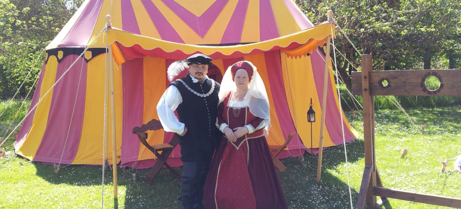 Two people in period costume standing in front of a yellow and red striped tent