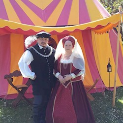 Two people in period costume standing in front of a yellow and red striped tent