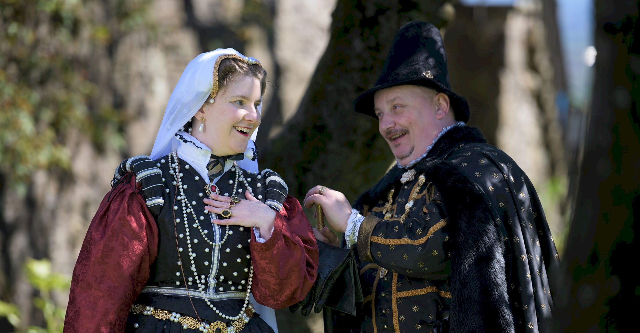 A man and lady in period costume surrounded by trees on a bright sunny day