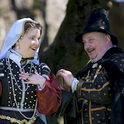 A man and lady in period costume surrounded by trees on a bright sunny day