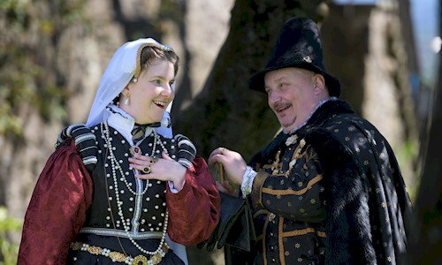 A man and lady in period costume surrounded by trees on a bright sunny day