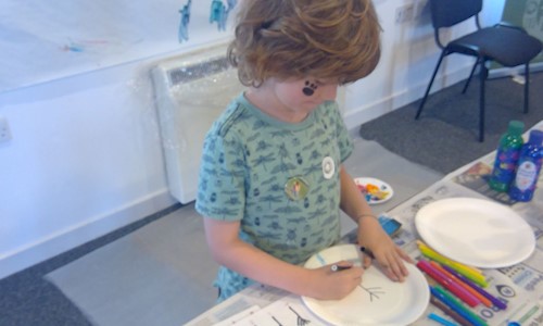 A boy with a paw print on his face and drawing on a paper plate