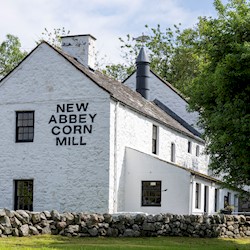 A white brick building with New Abbey Corn Mill painted on the end wall