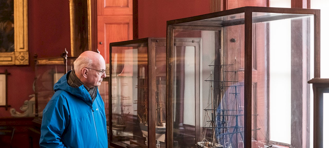 A man looking at a model ship in a glass case in the vast convening room at Trinity House