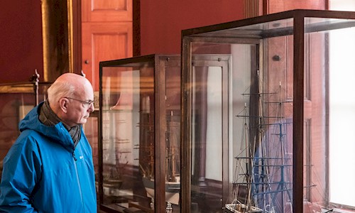 A man looking at a model ship in a glass case in the vast convening room at Trinity House