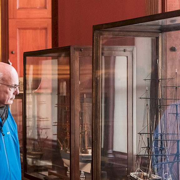 A man looking at a model ship in a glass case in the vast convening room at Trinity House
