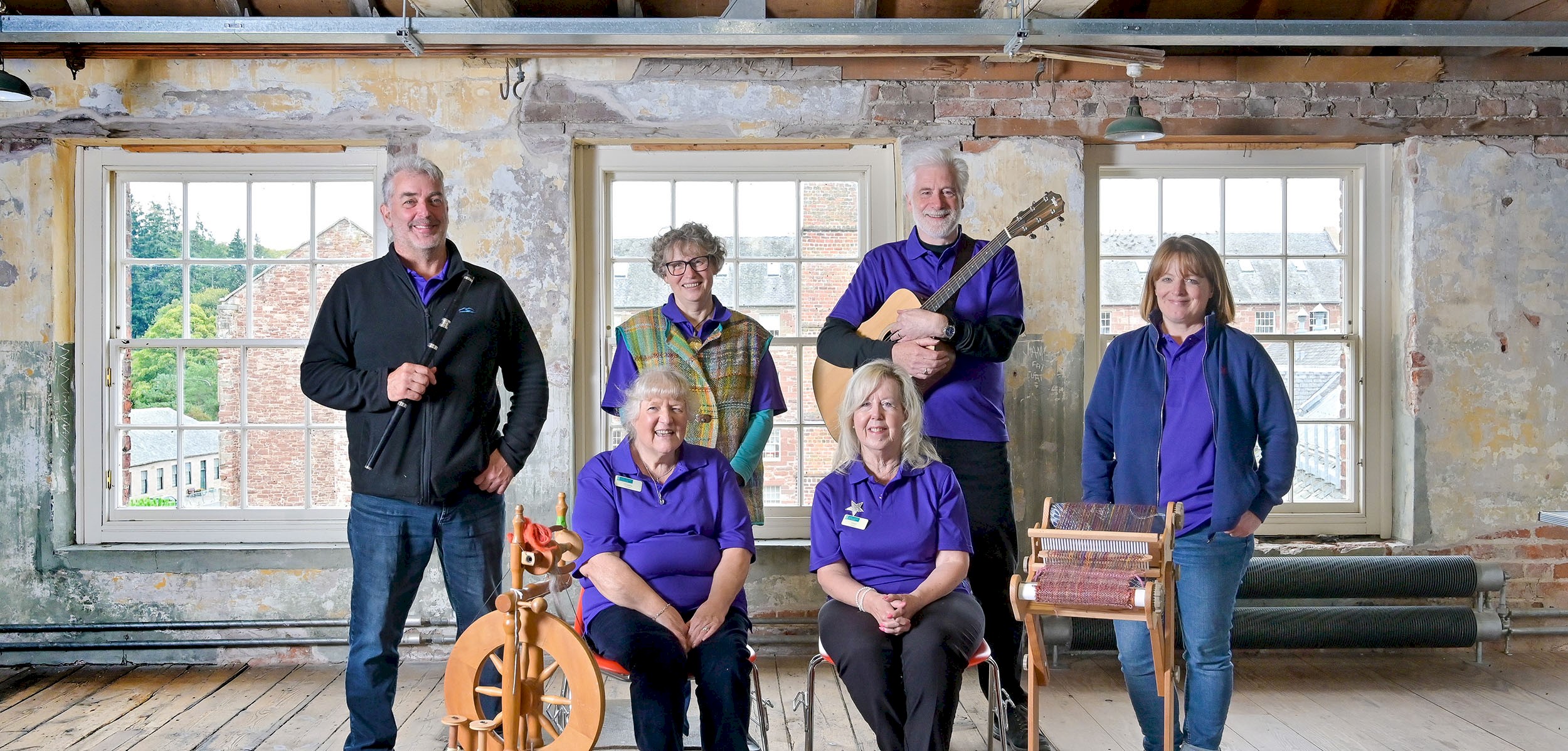 6 volunteers posing with a flute, guitar, spinning wheel and a weaving wheel