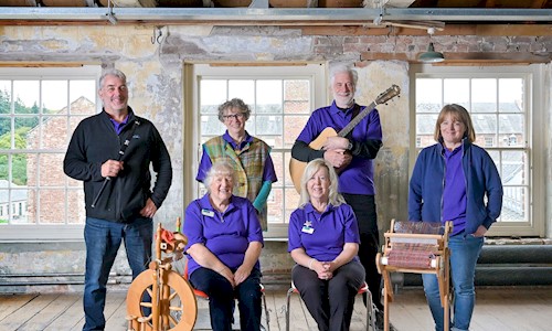 6 volunteers posing with a flute, guitar, spinning wheel and a weaving wheel