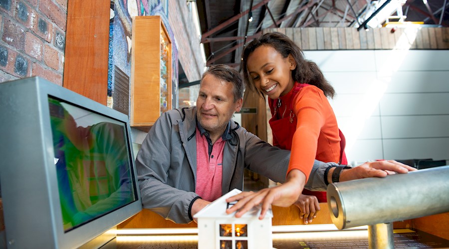 A child and a man smiling while interacting with a house exhibit inside the Engine Shed 