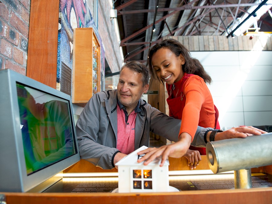 A child and a man smiling while interacting with a house exhibit inside the Engine Shed 